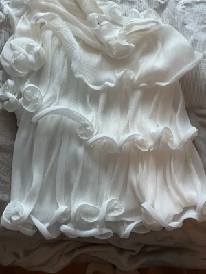 Vit omlottklänning med volanger - Superfin vit kortklänning med omlott-design och stora volangdetaljer. Klänningen har plisserat tyg och en oneshoulder-modell. Från NAKD endast använd en gång. 