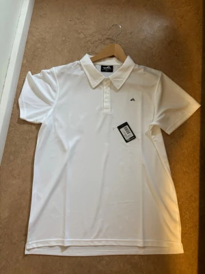 Vit pikétröja från Peak Performance - Klassisk vit pikétröja från Peak Performance med korta ärmar och krage. Tröjan har knappar framtill och en liten logga broderad på bröstet. Tillverkad i mjukt och lätt polyester, perfekt för en clean och sportig look.