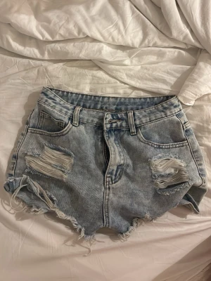 Ljusa low waist jeansshorts - Säljer ett par ljusblå jätte low waist jeansshorts med slitna detaljer och fransig kant. Shortsen har fem fickor, bälteshällor och dragkedja fram. Perfekta för en avslappnad och trendig look. Materialet är klassisk denim i bomull.