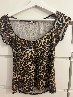 Leopardmönstrad topp med kort ärm - Snygg topp med leopardmönster i beige, brunt och svart. Modellen har korta ärmar och en rundad, något djupare urringning. Perfekt för dig som vill sticka ut lite extra. Materialet känns mjukt och följsamt mot huden.