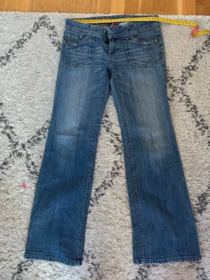Blå bootcut jeans från Fiveunits - Snygga blå bootcut jeans från Fiveunits med klassisk femficksmodell och slitningar på låren. Jeansen har normalhög midja, bälteshällor och metallknappar. Tillverkade i denim med en tvättad look som ger en avslappnad stil.