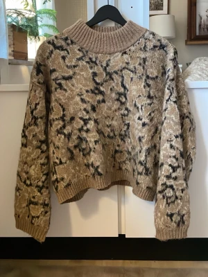 Stickad leopard tröja från Pieces - Stickad tröja från Pieces i beige med svart och mörkbrunt abstrakt mönster. Tröjan har en bred ribbad polokrage, ribbade muddar och avslut. Oversized passform och mjukt material som känns riktigt cozy. I storlek XS, har använts ett fåtal gånger på grund av att den är för kort i armarna  för mig. 