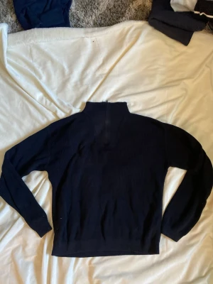 Svart ribbad stickad tröja Name It - Mörkblå eller svart ribbad stickad tröja från Name It med hög krage och half zip-dragkedja. Tröjan har lång ärm och en klassisk, enkel design som passar till det mesta. Perfekt för kyligare dagar och enkel att matcha.