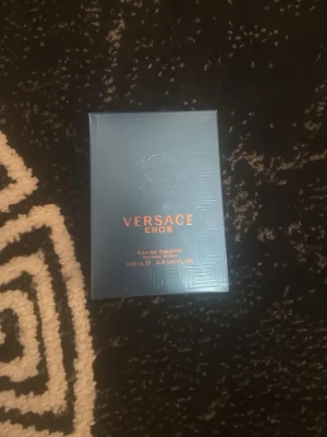Versace Eros Eau de Toilette 100 ml - Versace Eros Eau de Toilette i en elegant turkosblå glasflaska med guldigt lock och Medusa-motiv. Förpackningen är turkosblå med metallicdetaljer och text i guld. Flaskan rymmer 100 ml och har en lyxig, modern design som verkligen sticker ut.