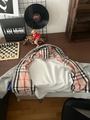 Burberry Hoodie - Snygg grå zip-hoodie från Burberry med klassiskt rutigt foder i huvan. Hoodien har dragkedja framtill, två fickor och ribbade muddar. Perfekt för dig som vill ha en stilren look med en touch av lyx.