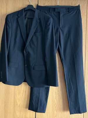 Riley Tvådelad kostym - Säljer en helsvart kostym med kavaj och byxor från Riley, köpt på Brothers. I fint skick, endast använd ett fåtal gånger. Både kavaj och byxor är i storlek 48. Tailored fit.   Perfekt till bröllopet, studenten eller examen.