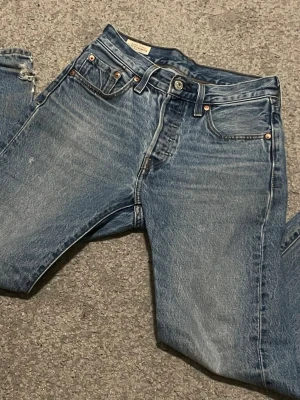 Levi's Premium 501 blå raka jeans - Snygga blå Levi's Premium 501  jeans med klassisk femficksmodell och raka ben. Jeansen har en vintage tvättad look med kontrastsömmar och metallknappar. Tillverkade i slitstark denim som ger en tidlös och avslappnad stil.
