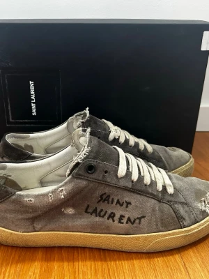 Grå Saint Laurent sl/06  - Saint Laurent i modellen sl/06. Storlek 40 sitter som 41/41.5. Har ett antal små deffekter som går att fixa. Allt og medkommer:Box, dustbags, äktahets bevis osv. Nypris 7000kr, bara att höra av sig vid frågor. 