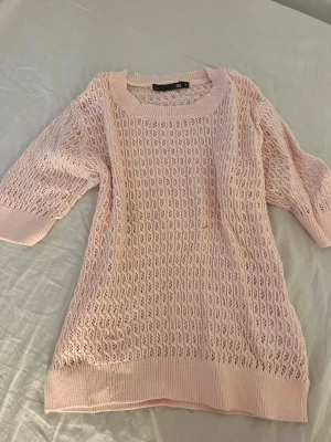 Ljusrosa stickad tröja - Söt ljusrosa stickad tröja med halvtransparent hålmönster och rund halsringning. Tröjan har trekvartsärmar och ribbade muddar vid ärmslut och nederkant. Endast använd en gång