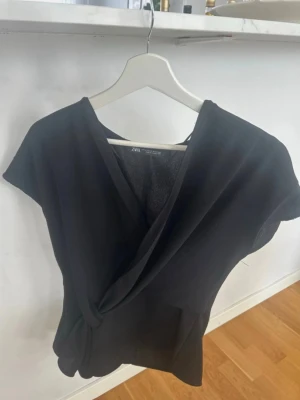 Svart omlottopp från Zara - Jätte jättesnygg svart omlottopp från Zara med v-ringning och korta ärmar. Använd sparsamt utan några defekter. Pris kan diskuteras❣️❣️