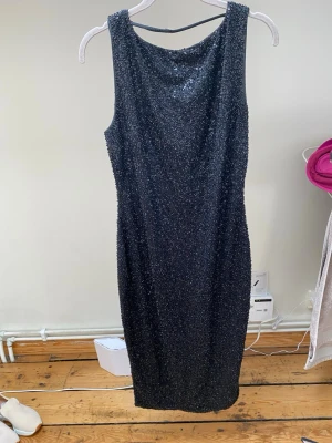 Glittrig klänning från Oh Polly - Snygg svart glittrig klänning med ärmlös design och öppen rygg. Klänningen är figurnära och har en klassisk, rak siluett som slutar ovanför knäna. Perfekt för dig som vill sticka ut med lite extra glitter. Storlek uk 14