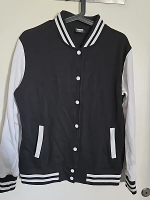 Svart och vit collegejacka Urban Classics - Snygg svart och vit collegejacka/baseballjacka från Urban Classics i storlek XL men upplevs mer som strl L. Jackan har vita ärmar, svarta och vita muddar samt knappar framtill. Klassisk basebollstil med randig krage och fickor med vita detaljer. Köpt på EMP & nypris va 649:-