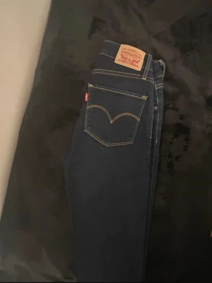 Mörkblå Levi's skinny jeans. - Snygga mörkblå jeans från Levi's med skinny passform och kontrastsömmar. Jeansen har fem fickor, Levi's ikoniska läderpatch bak och röd etikett på bakfickan.