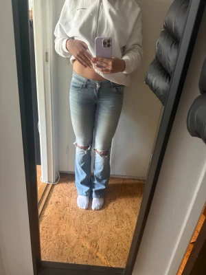 Nelly Ljusblå slitna bootcut jeans - Säljer ett par ljusblå bootcut jeans med slitningar vid knäna och lätt tvättad look 
