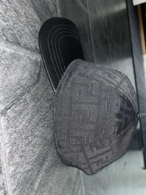 Svart Fendi keps med FF-mönster - Snygg svart keps från Fendi med det klassiska FF-logomönstret över hela tyget. Skärmen är i svart läderlook med vita sömmar som ger en clean kontrast. Perfekt accessoar för dig som gillar exklusiv streetwear och vill sticka ut.