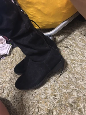 Svarta overknee stövlar i mockaimitation - Säljer ett par svarta overknee stövlar med snörning upptill. Stövlarna har låg klack och är gjorda i mockaimitation som ger en mjuk och stilren look. Perfekta till höstens och vinterns outfits.