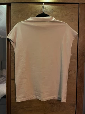 Beige polotopp i bomull - Enkel och stilren beige polotopp med korta ärmar. Toppen har en mjuk krage och är tillverkad i bomull. Ny utan prislapp. Aldrig använd