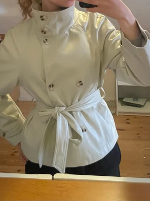 High neck short jacka I konstläder  - Kort jacka som är perfekt till våren. Kort trenchcoat i konstläder som är använd en gång. Har en hög krage som kan vikas ner. Pris kan diskuteras 💗