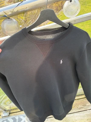 Svart sweatshirt från Polo Ralph Lauren - Klassisk svart sweatshirt från Polo Ralph Lauren med rund halsringning och diskret broderad logga på bröstet. Tröjan har ribbade muddar vid ärmslut och nederkant. Perfekt basplagg för en clean och stilren look. Använd ett fåtal gånger och är i fint skick, skriv vid minsta fundering🙌🏻🙌🏻