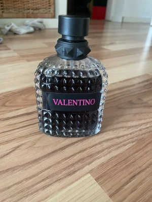 Valentino parfym  - Parfym från Valentino i en cool, nitprydd glasflaska med svart och transparent design. Flaskan har en svart etikett med rosa text och ett svart lock med dekorativa detaljer. 