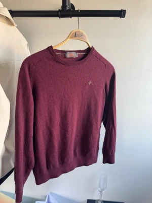 Bordeaux stickad tröja från Morris - Snygg bordeaux stickad tröja från Morris med rund halsringning och diskret logga broderad på bröstet. Tröjan har långa ärmar och ribbade muddar vid ärmslut och nederkant. Perfekt för lager-på-lager-stil.