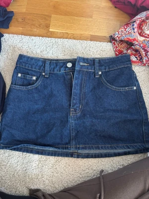 Mörkblå jeanskjol från SHEIN - Snygg mörkblå jeanskjol från SHEIN i klassisk femficksmodell. Kjolen har knapp och dragkedja framtill samt kontrastsömmar. Perfekt till vardags för en trendig look.