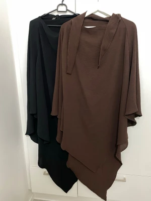 Brun och svart khimar - Två st khimar  i brun och svart med lös passform och asymmetrisk nederkant. Ganska långa och passar perfekt med vilken abaya som helst. Kommer i fin skick utan skador