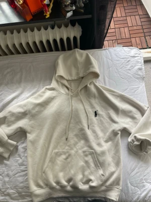 Vit hoodie från Polo Ralph Lauren - Säljer en stilren vit hoodie från Polo Ralph Lauren med klassisk broderad logga på bröstet. Hoodien har dragsko i huvan och en stor magficka. Tillverkad i mjukt bomullsmaterial och har ribbade muddar vid ärmslut och nederkant.