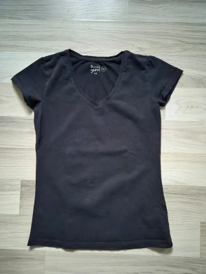 Svart v-ringad t-shirt Basic You - En enkel svart t-shirt från Basic You med v-ringning och korta ärmar. Tillverkad i mjuk bomull och har en normal passform som sitter snyggt på kroppen. Perfekt basplagg till garderoben.
