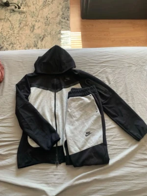 Nike mjukisbyxor svart och grå - Snygga mjukisbyxor från Nike i svart och ljusgrått med elastisk midja och sidofickor. Byxorna har en sportig look med kontrastpaneler och Nike-logga på benet. Perfekta för chill eller träning.