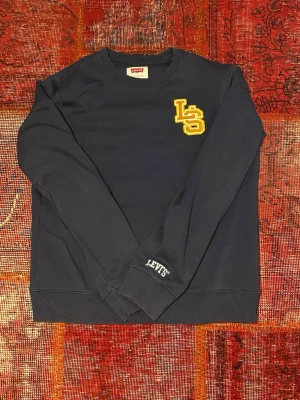 Levi’s hoodie  - Mörkblå sweatshirt från Levi's med gul LS-logga på bröstet och Levi's-tryck på ärmen. Klassisk rund halsringning och ribbade muddar. Perfekt för en avslappnad och stilren look.