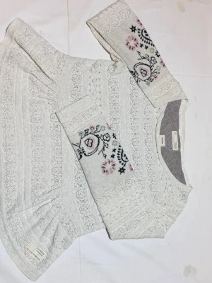 Odd Molly tröja  - Supersöt vit stickad tröja från Odd Molly med spetsmönster och broderade detaljer i rosa och svart på ärmarna. Tröjan har rund halsringning och långa ärmar. Perfekt för dig som gillar romantisk och bohemisk stil.