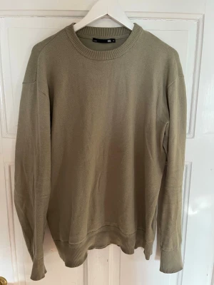 Grön stickad tröja från 157 - En stilren grön stickad tröja från 157 med rund halsringning och ribbade muddar vid ärmslut och nederkant. Perfekt för lager-på-lager och enkel att matcha med jeans eller chinos.