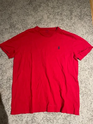 Röd t-shirt från Polo Ralph Lauren - Klassisk röd t-shirt från Polo Ralph Lauren med rund halsringning och liten broderad logga på bröstet. Perfekt basic-plagg med avslappnad passform och korta ärmar.