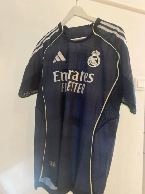 Real Madrid Bellingham matchtröja #5 - Mörkblå Real Madrid matchtröja från Adidas med Bellingham och nummer 5 på ryggen. Tröjan har vita och ljusgula detaljer, klubbmärke och sponsortryck framtill samt Champions League-märke på ärmen. Tillverkad i lätt och ventilerande funktionsmaterial.💙💙💙