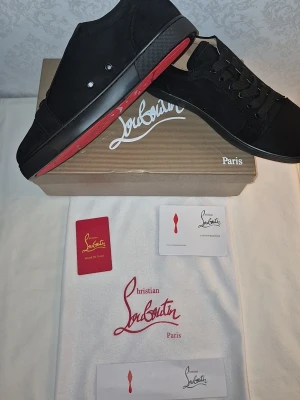 Svarta sneakers från Christian Louboutin - Snygga svarta sneakers från Christian Louboutin med klassisk röd sula. Skorna har en stilren design i svart mocka och textil, svarta skosnören och diskreta detaljer. Perfekta för dig som gillar exklusiva och trendiga sneakers med ikonisk look.