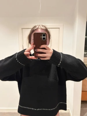 Svart oversized stickad tröja - Säljer en svart stickad tröja med vita detaljer vid ärmslut, halsringning och nederkant. enbart testad, aldrig använd. köpt för 900 kr