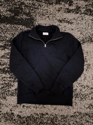 Svart half-zip sweatshirt - Stilren svart sweatshirt från Volt med half-zip och hög krage. Tröjan har långa ärmar, ribbade muddar och är gjord i mjukt bomullsmaterial. Perfekt för en avslappnad och trendig look.