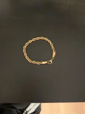 Guldtonat tvinnat armband - Snyggt armband i guldtonad metall med tvinnad kedja och klassisk karbinhake. Armbandet har en stilren och tidlös design som passar perfekt till olika stilar. Inget synligt märke på armbandet.