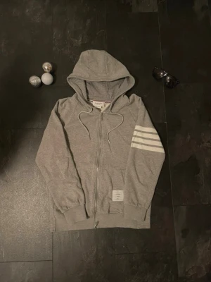 Thom Browne hoodie - Säljer en zip hoodie från Thom Browne i storlek 2 vilket motsvarar S/M. Den är i väldigt bra skick och kan fraktas snabbt