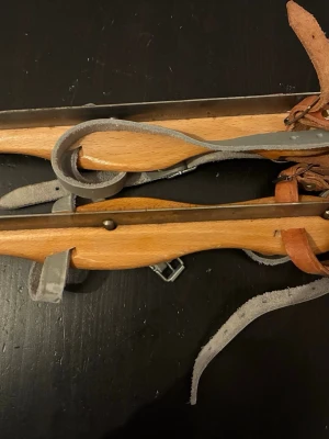 Nijdam träskridskor med läderremmar - Klassiska träskridskor från Nijdam med robusta läderremmar och metallskena. Skridskorna har en naturlig träfärg med detaljer i rött och svart på sidan samt tydlig logga. Perfekta för dig som gillar retrostil och vill sticka ut på isen.