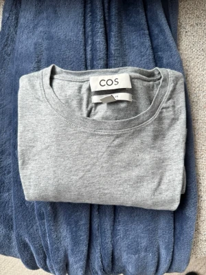 Grå basic t-shirt från COS - En stilren grå t-shirt från COS i mjuk bomull. Klassisk rund halsringning och normal passform. Perfekt till jeans eller shorts för en enkel och clean look.