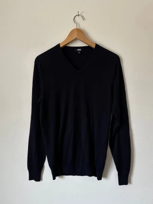 Mörkblå V-ringad stickad tröja Uniqlo - Klassisk mörkblå stickad tröja från Uniqlo med V-ringning och långa ärmar. Tröjan har en enkel och stilren design med ribbade muddar vid ärmslut och nederkant. Perfekt basplagg i garderoben och lätt att matcha till olika outfits. 8B17