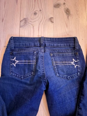 G-rise jeans - Säljer ett par mörkblå jeans från G-Rise med unika vita stjärndetaljer på bakfickorna. Klassisk femficksmodell med raka ben och snygg tvätt. Perfekta för dig som vill ha något extra i din denimlook.