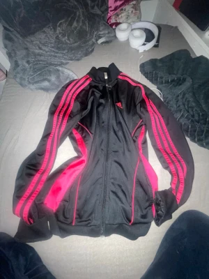 2000s Adidas kofta - En svart och rosa sportig adidas kofta som ger lite 2000s vibar och som är lite baggy och har fickor. Den är XS men skulle säga att den passar som S mer. Säljer den eftersom att den är lite för stor för mig.