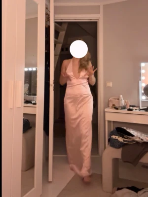 Peppermayo Balklänning - Säljer en elegant ljusrosa långklänning med djup v-ringning och smala axelband. Klänningen har en figurnära passform och är i satin, Perfekt för speciella tillfällen. Klänningen är helt ny med prislappar och påse kvar, aldrig använd bara provad och klänningen har en gömd dragkedja vid ena sidan för att lätt kunna ta på och av sig klänningen men samt kunna justera ryggbandet till sin passform!🥰