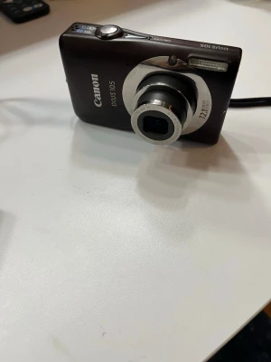 Canon IXUS 105 digitalkamera brun - Snygg brun Canon IXUS 105 digitalkamera med 12,1 megapixlar och kompakt design. Kameran har en tydlig LCD-skärm, silverfärgat objektiv och medföljer gör ett batteri samt ett 32GB SD-kort. Perfekt för dig som vill ha en smidig kamera att ta med överallt.