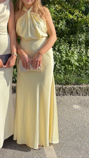 Ljusgul lång klänning med halterneck - Säljer denna superfina ljusgula långklänning med halterneck. Perfekt för bal eller student. Materialet är rejält och känns ordentligt. Har använt en gång och då fick den en liiiten fläck men inget man märker💞 Bär vanligtvis XS/S så stor för att vara XXS. Är 165 men hade 8 cm klack på balen och den gick precis ner till marken💞