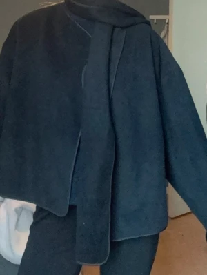 Svart kappa med scarf - Stilren svart kappa med rak passform och scarf. Kappan har en minimalistisk design som ger en lyxig känsla. Enkel att matcha med olika outfits.