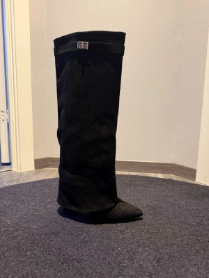 Svarta höga stövlar med klack - Säljer ett par svarta höga stövlar i mockaimitation med spetsig tå och hög klack från Raglady. Stövlarna har ett dekorativt spänne upptill och dragkedja på insidan. Använda endast ett fåtal gånger.